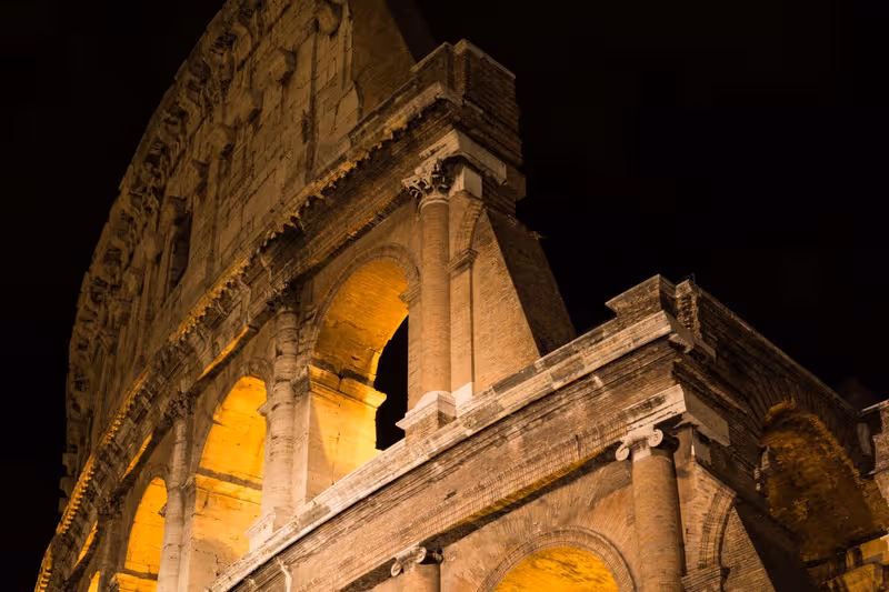 The Colosseum illuminated at night, showcasing its grand arches against the dark sky.